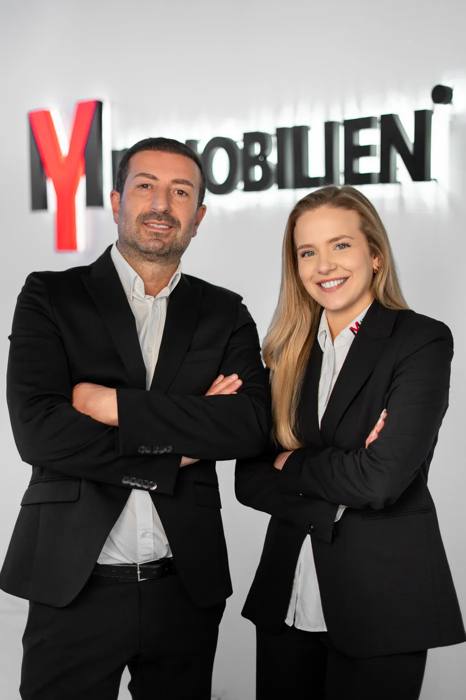 Zwei Mitarbeitende vor der Logowand von MY Immobilien